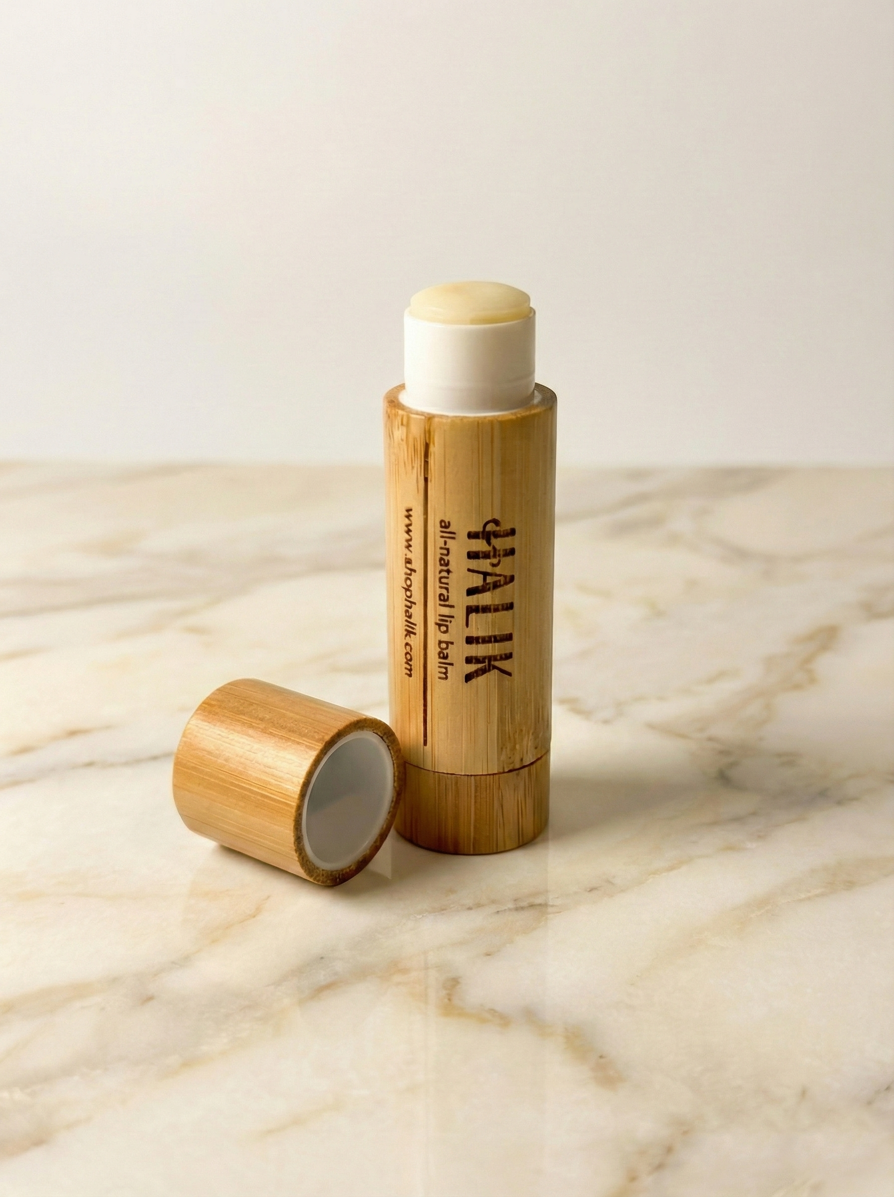 A bamboo container of all-natural lip balm with the lid off, placed on a marble surface with a plain white background.