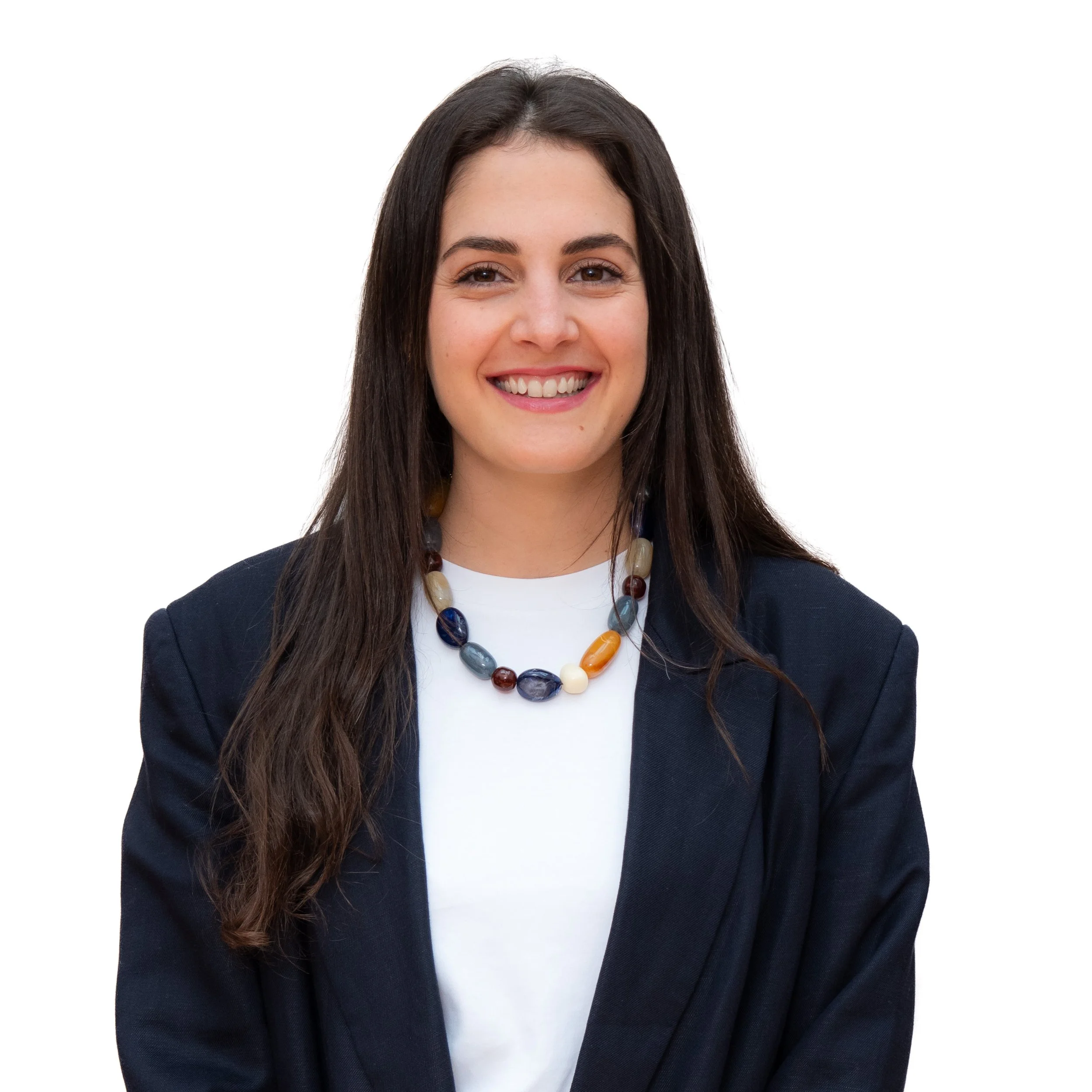 Headshot of a woman with long, dark hair smiling, wearing a black blazer and a colorful beaded necklace against a white background.