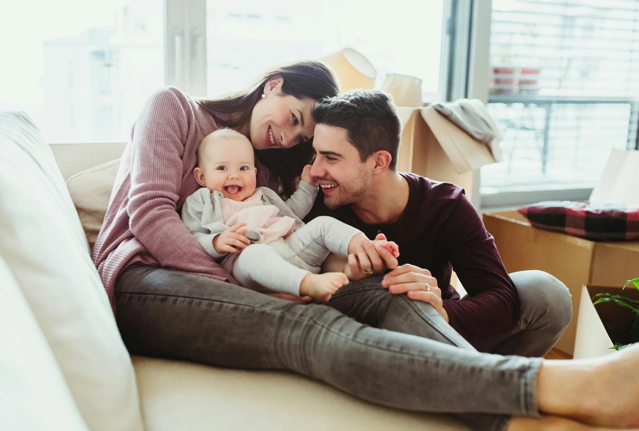 A happy couple enjoys time with their baby on the couch. They are both more able to engage in parenting tasks because of the work they did together in couples therapy at Heights Couples Therapy in Houston.