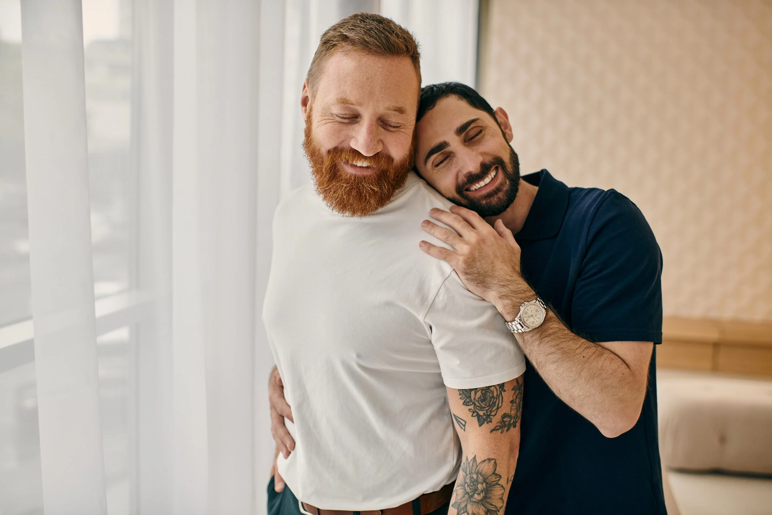 Two men embracing in a bright home, representing inclusive support from a couples therapist Houston and relationship therapist Heights services.
