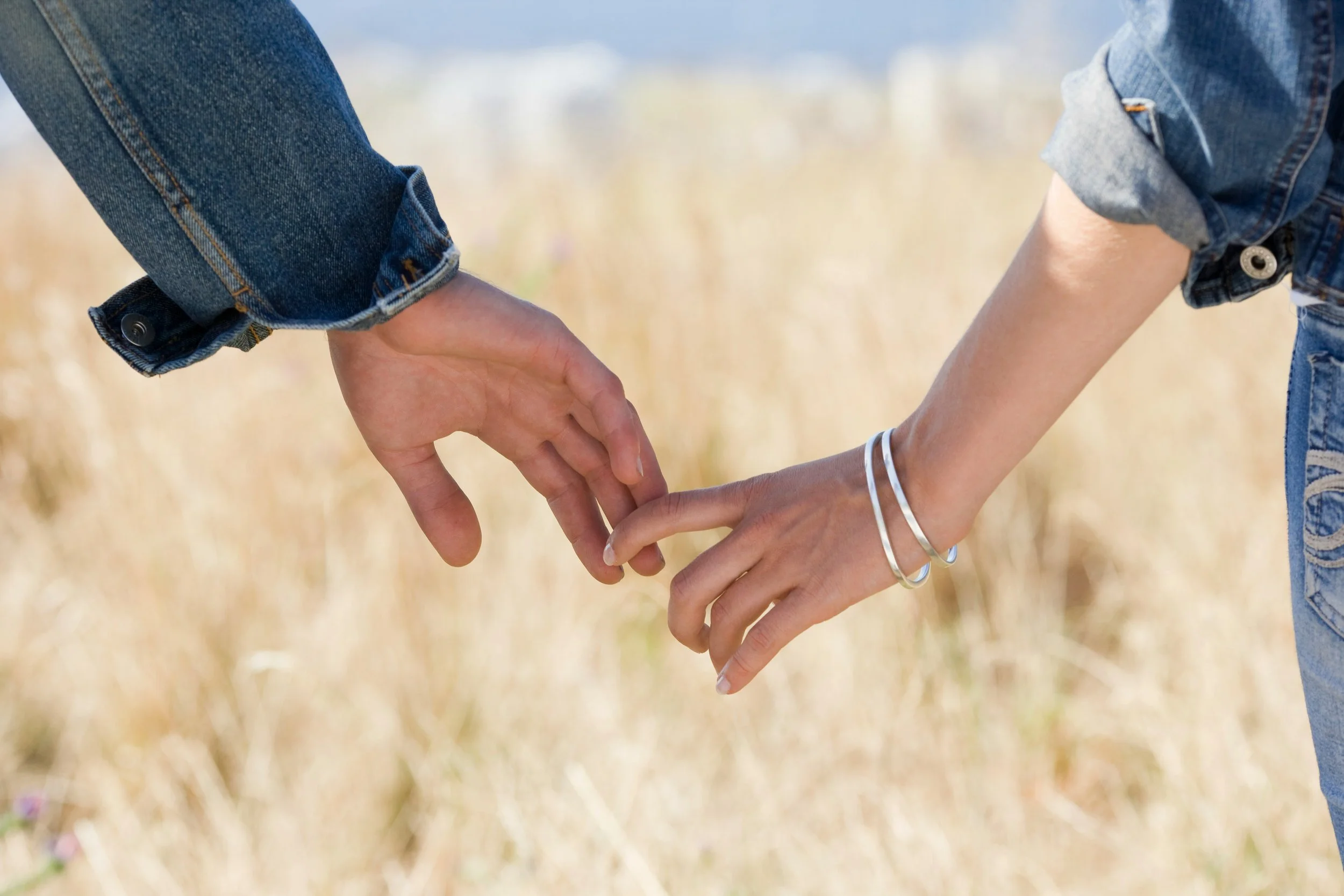 A couple holding hands but about to let go. One partner is struggling with the other partner's anxiety or addiction, and is looking into Houston-based individual relationship therapy since their partner refuses therapy.