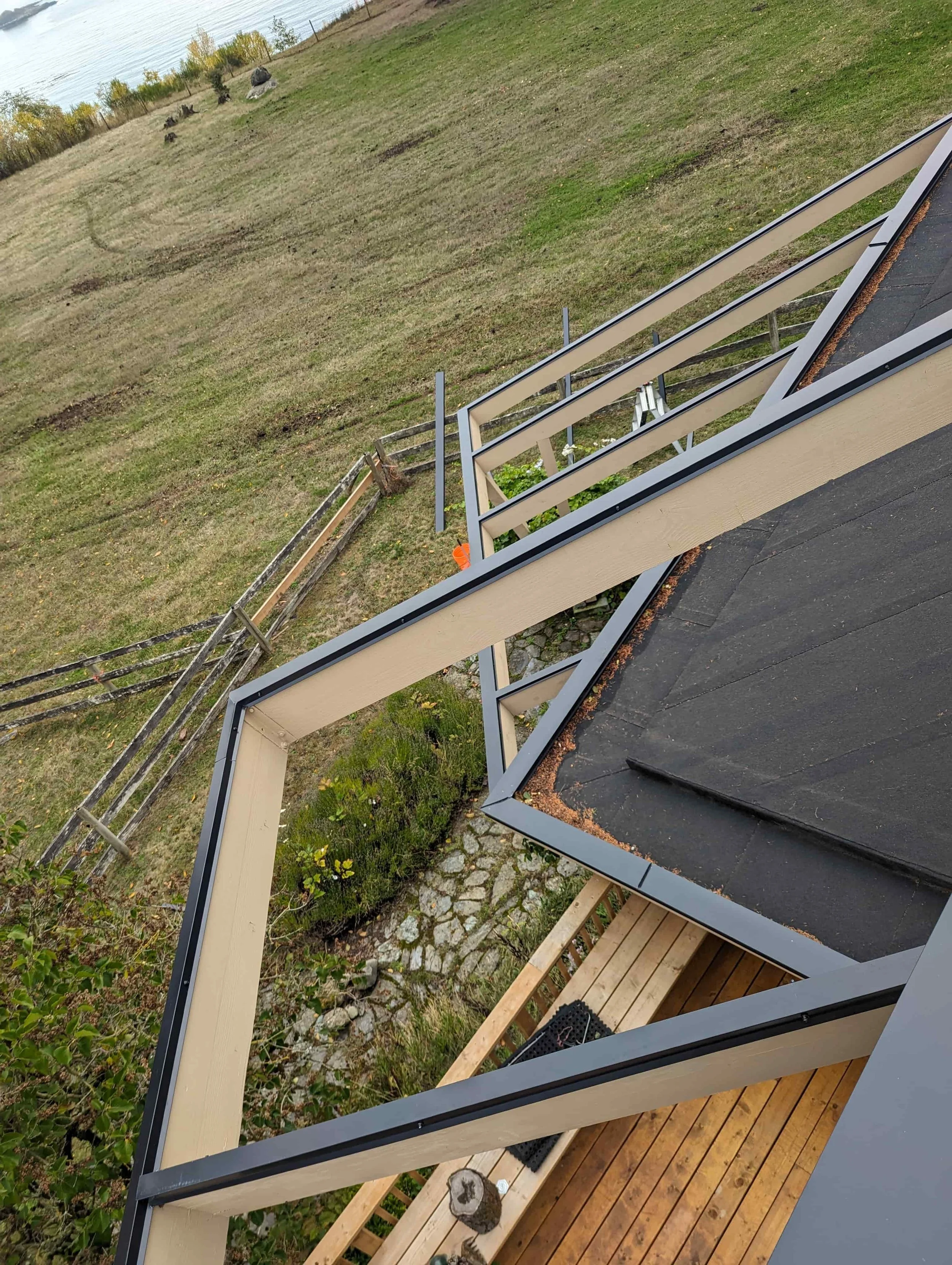 View looking down from a balcony showing a grassy yard with trees, a wooden fence, stone pathway, and overcast sky.