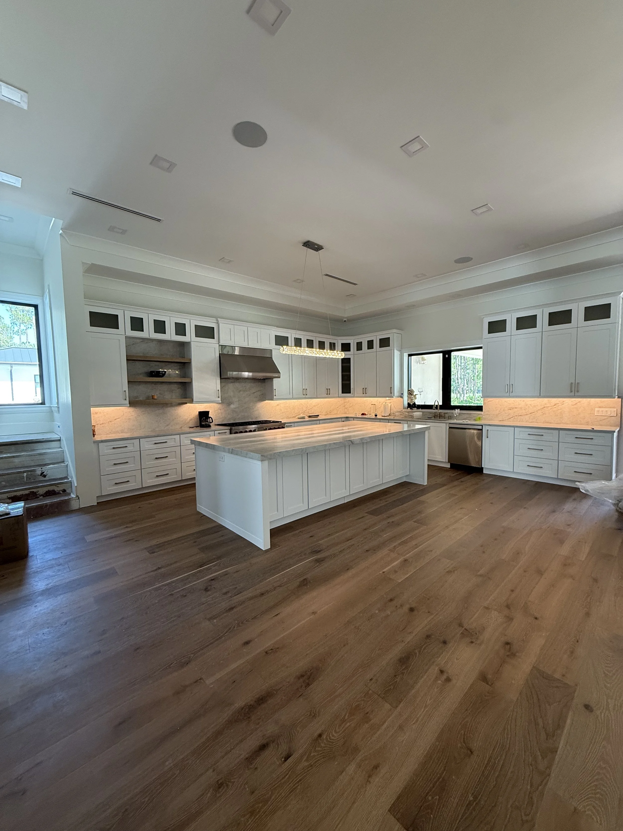 Modern white kitchen with island, stainless steel appliances, gray and white backsplash, gray countertops, and wooden flooring.