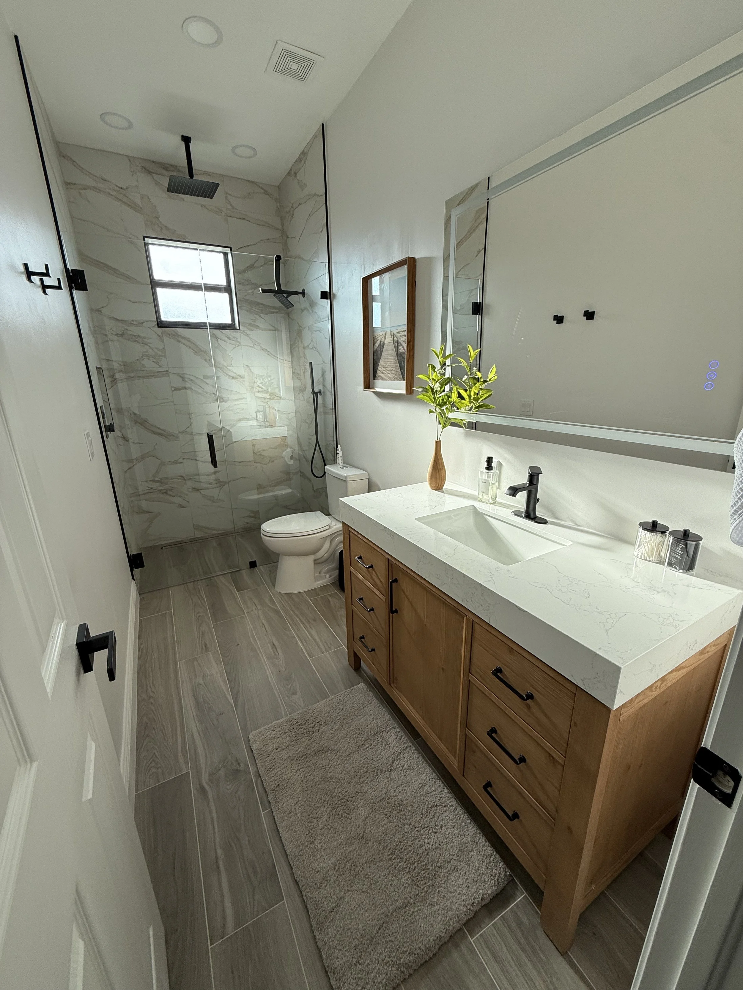 Modern bathroom with a clawfoot bathtub, large mirror with cabinets, white marble countertop, chandelier, and wall sconces, with white plantation shutters on the windows.