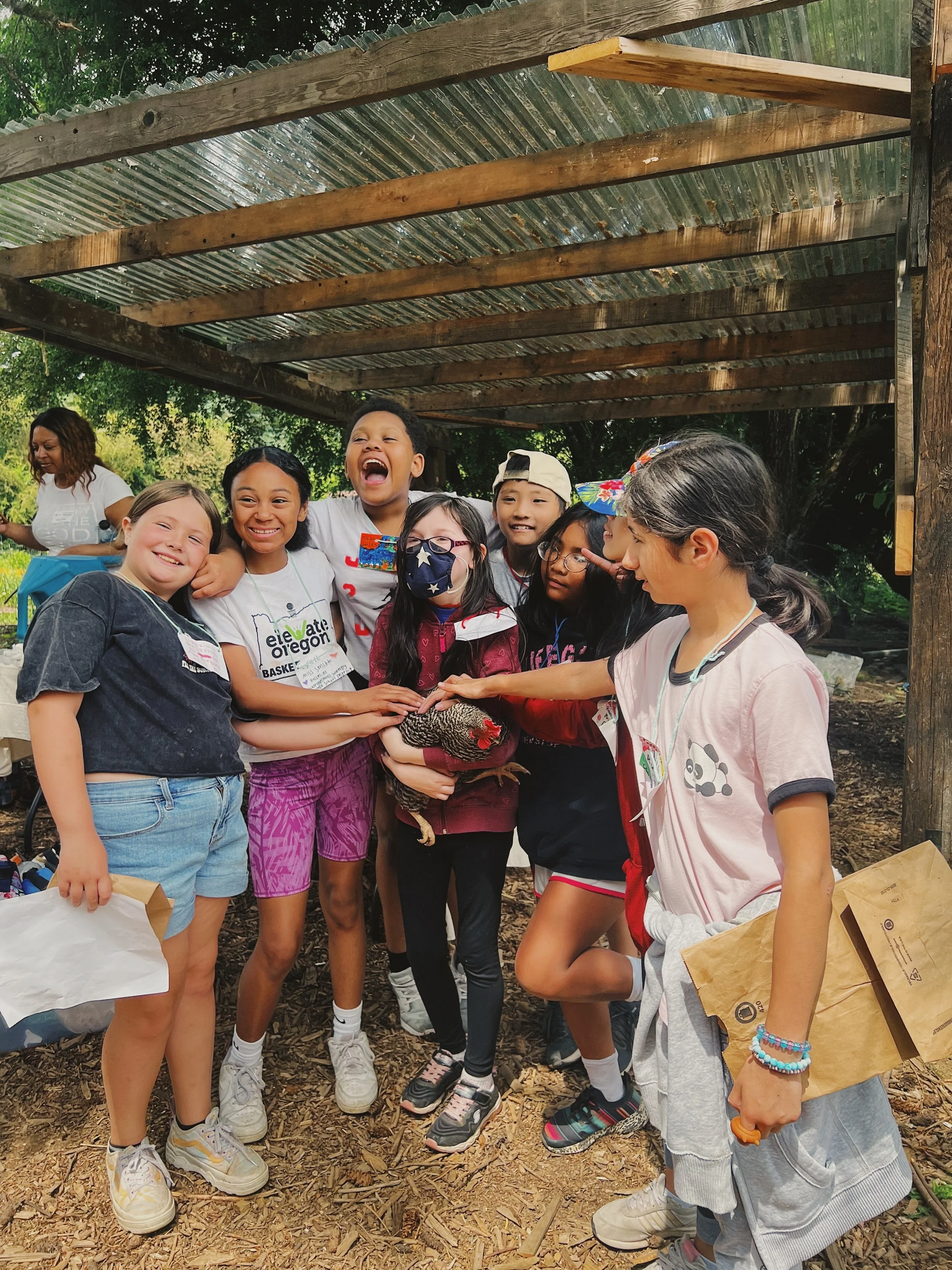 A child holding a chicken, surrounded by other happy children petting the chicken and posing for the camera