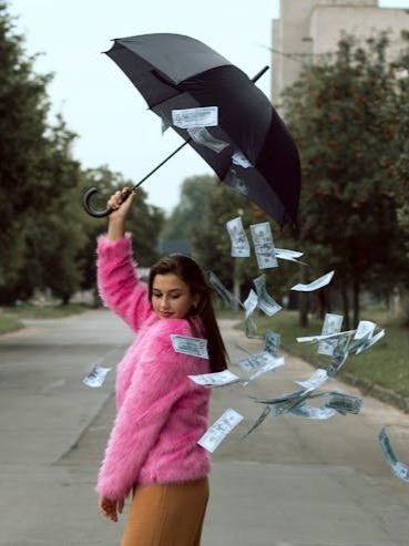 Woman holds umbrella while it rains money, symbolizing helping therapists make more money.