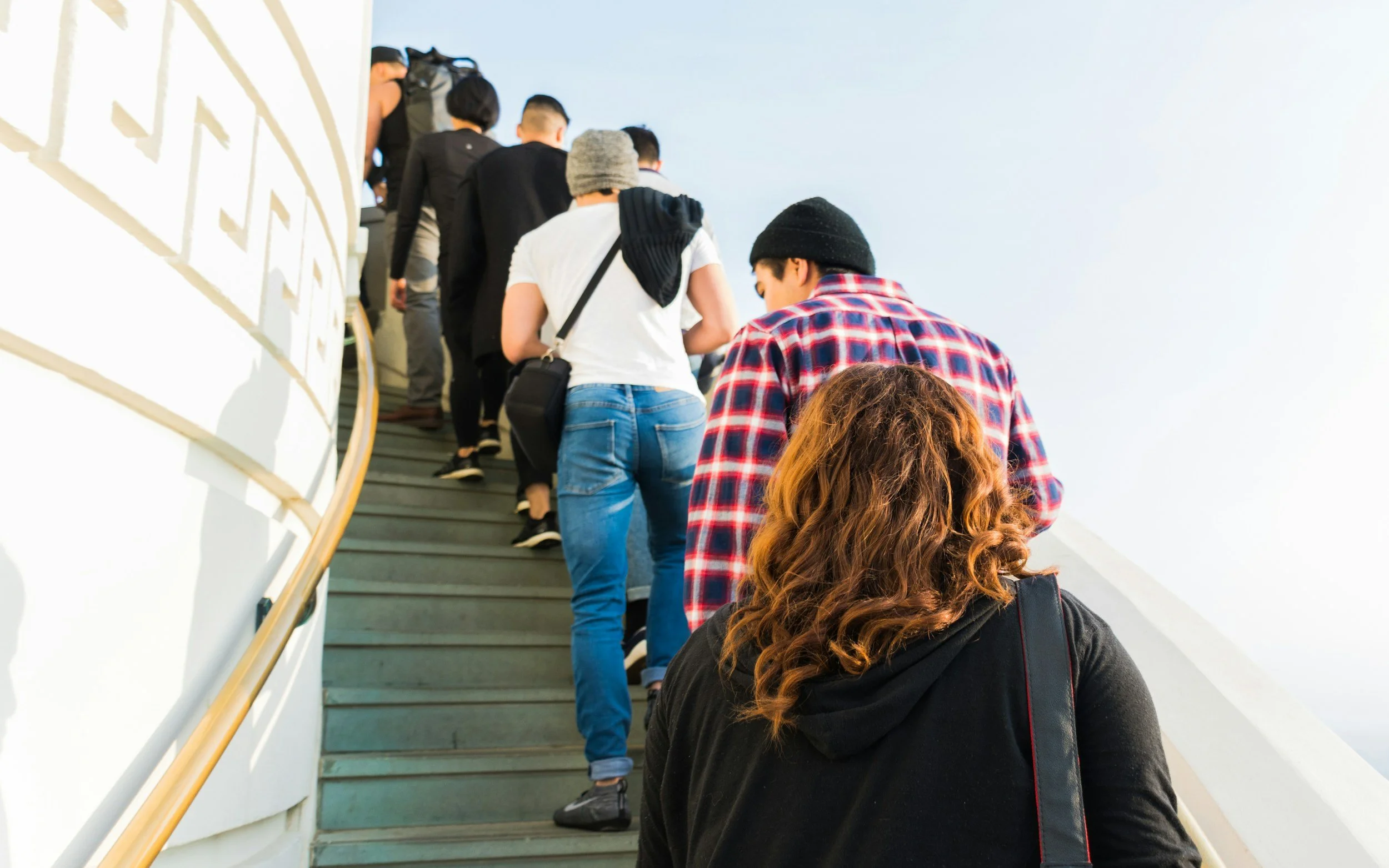 People standing and walking up an outdoor staircase with a curved white wall on the side.