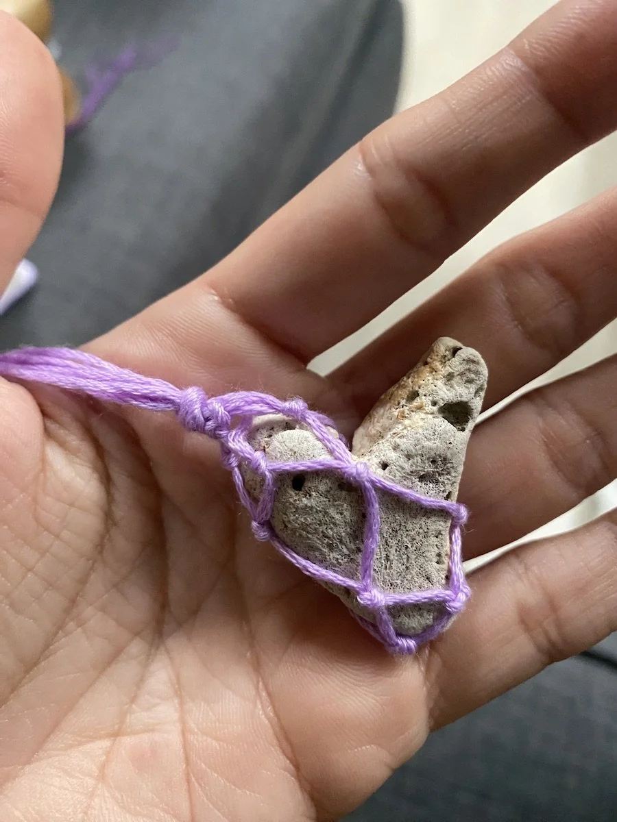 Hand holding a small, porous rock wrapped in purple string or netting.