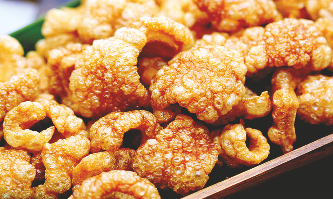 Golden brown pork rind pieces served in a wooden dish.