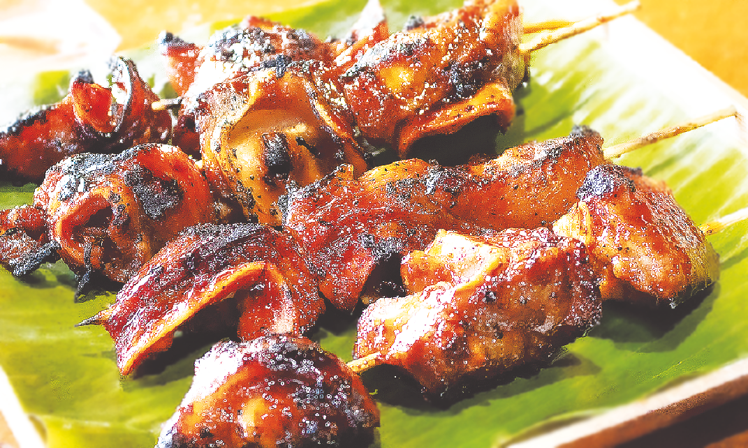 Skewers of grilled marinated pork ears served on a banana leaf platter.