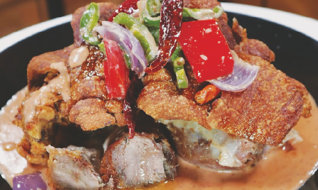 Deep‑fried pork hocks or belly in spicy coconut sauce with shrimp paste, onions, bell peppers, and tomatoes