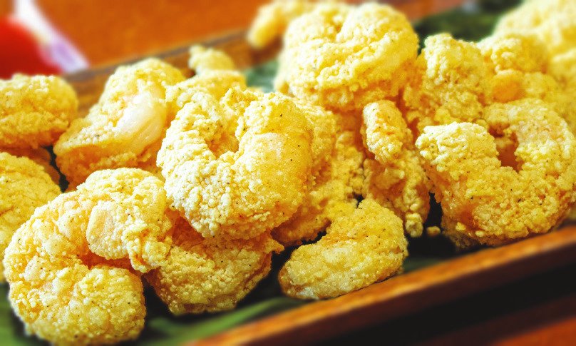 Crispy deep-fried popcorn shrimp piled on a wooden plate..
