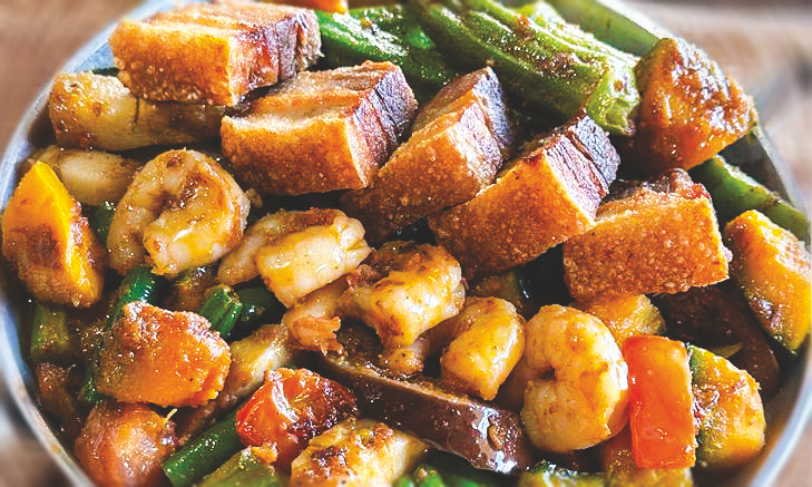 A bowl of sautéed green beans, squash, okra, bitter melon, and eggplant in shrimp paste, topped with pork belly chunks and shrimp.