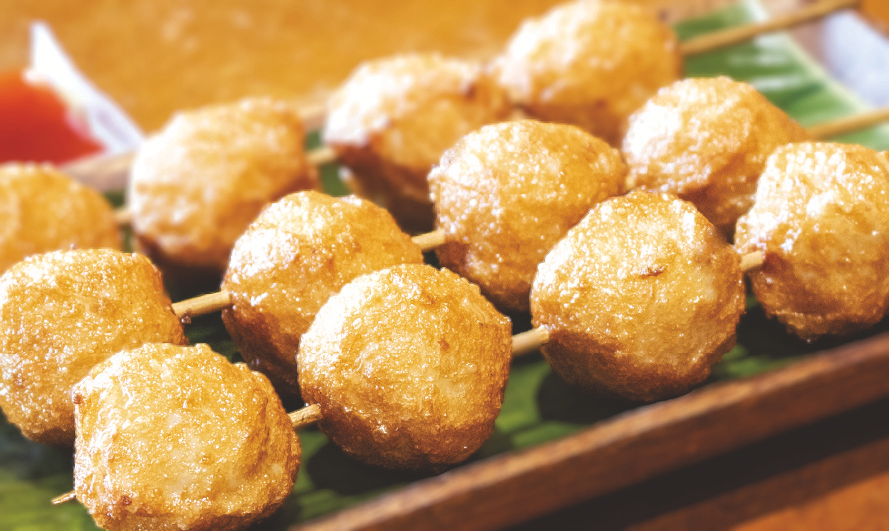 Deep-fried squid balls with a golden crust served on a green leaf platter.