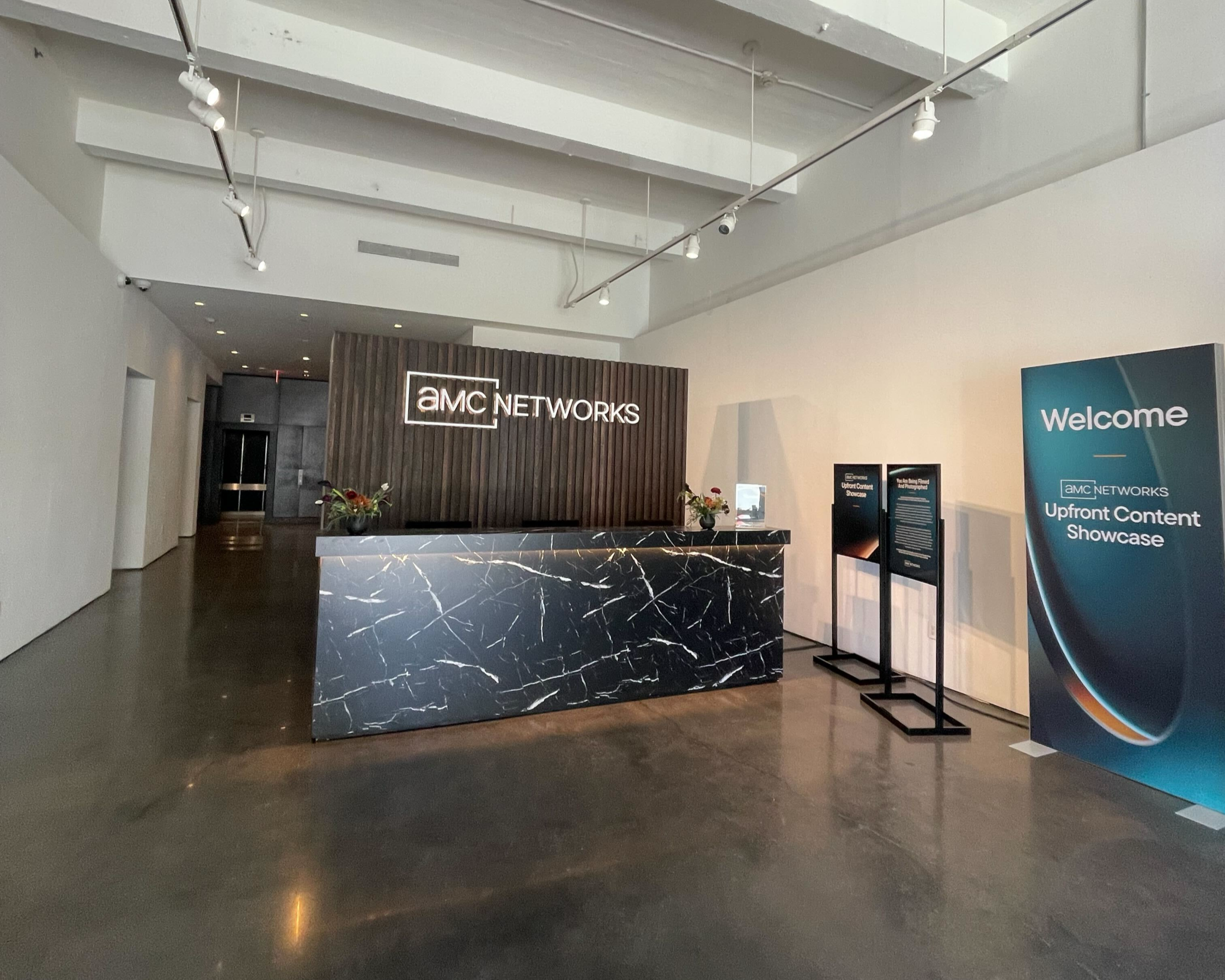 Custom welcome desk with inset lighting on surface overhang against slatted wood backwall with dimensional lettering