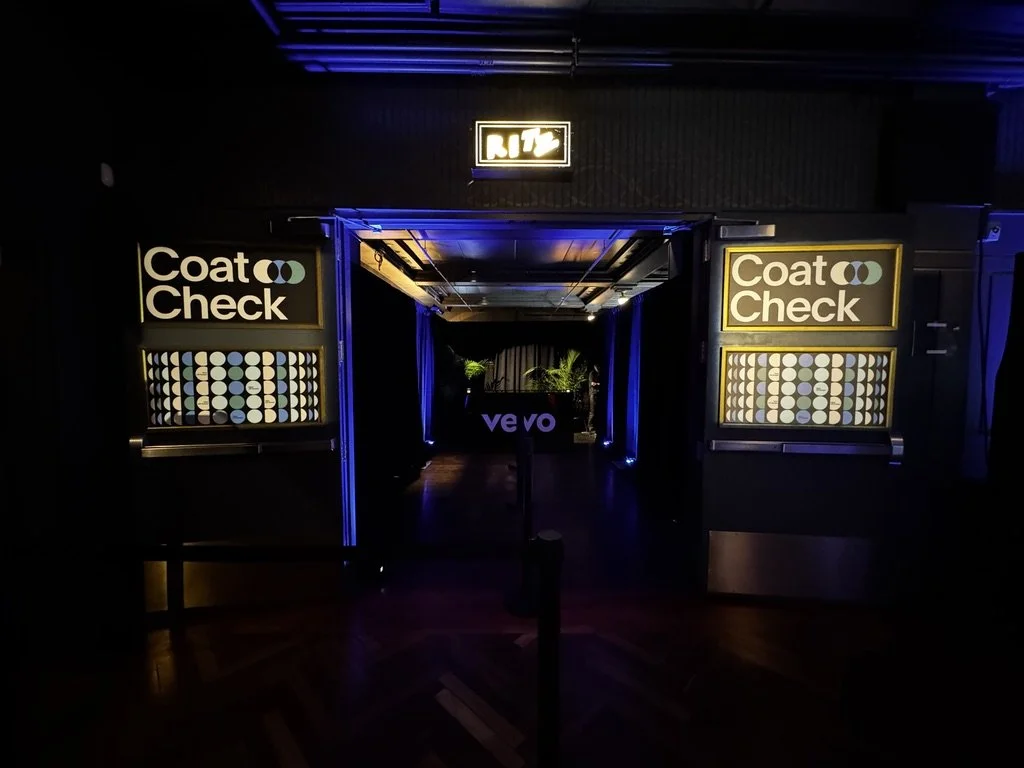 Strategically placed graphics inset against existing venue architecture. In the background, branded coat check desk with some added plants.