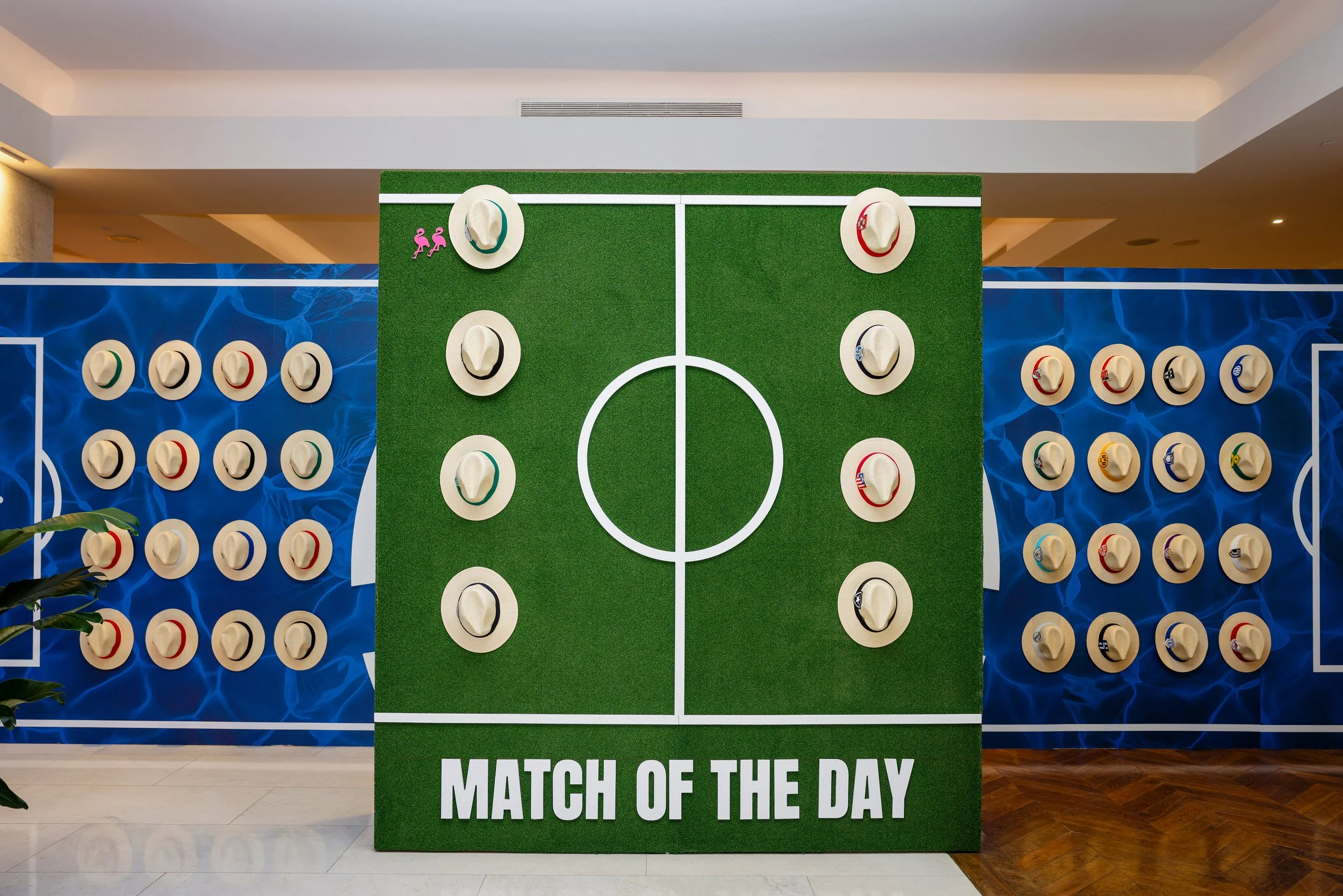 On the backside of the welcome wall, featured a water graphic on the background against hats with team crests and matching colors on the hat band. Interactive turf wall displayed points via flamingos next to team hat. (Grand Beach Hotel; Miami, FL)