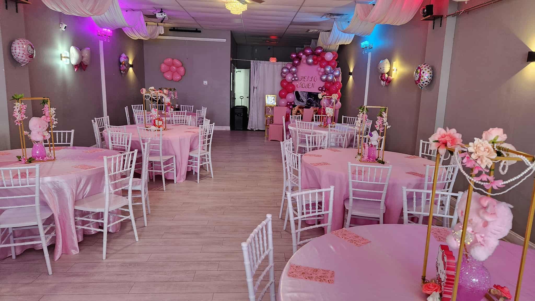 Decorated event space for a child's birthday with pink themed tables, balloons, and wall decorations.
