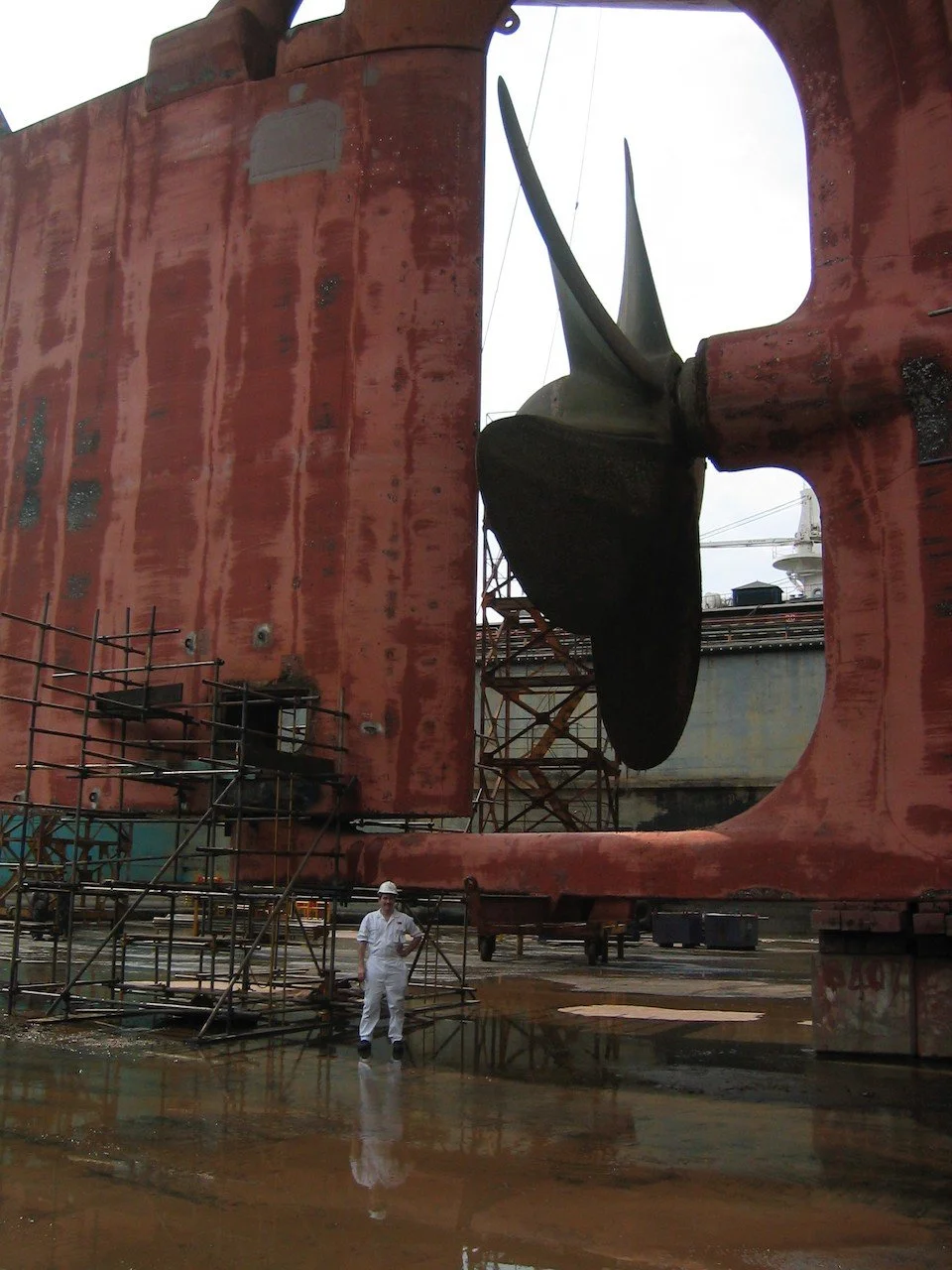 Shawn Isakson in white coveralls and a hard hat beside a ship's hull and propeller in a dry dock in Johor Bahru, Malaysia, on an ExxonMobil project delivering FSO vessels to fields in West Africa