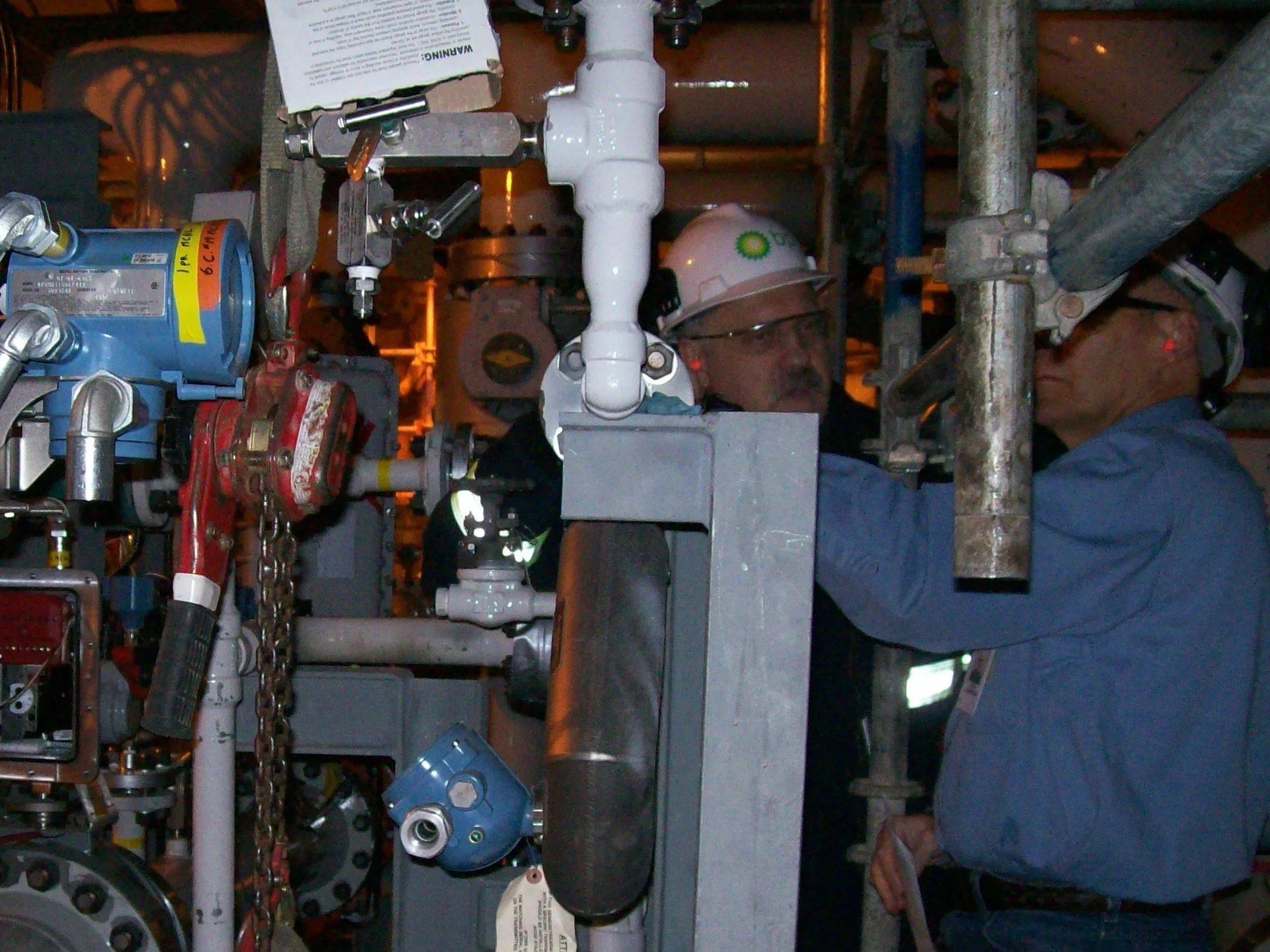 Two workers in hard hats, one with a BP logo, among valves, piping and instruments inside a BP facility at Prudhoe Bay, Alaska, 2008