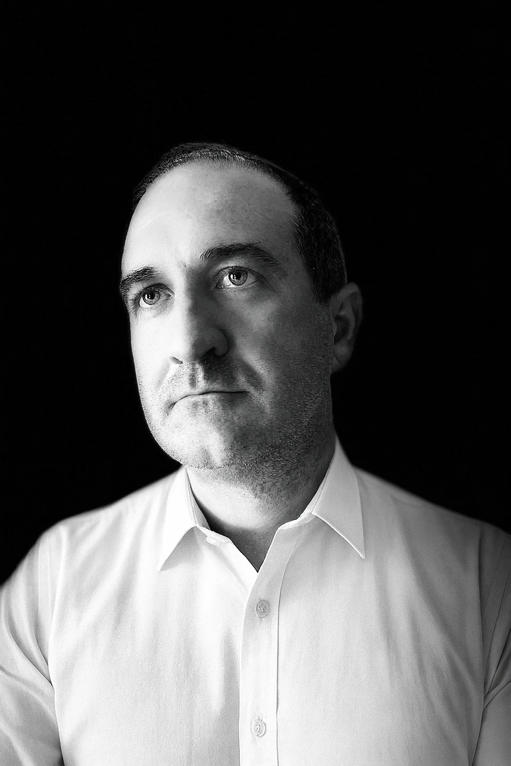 Black-and-white portrait of Shawn Isakson, interim CEO and COO, in an open-collar white shirt against a dark background, looking off to the side