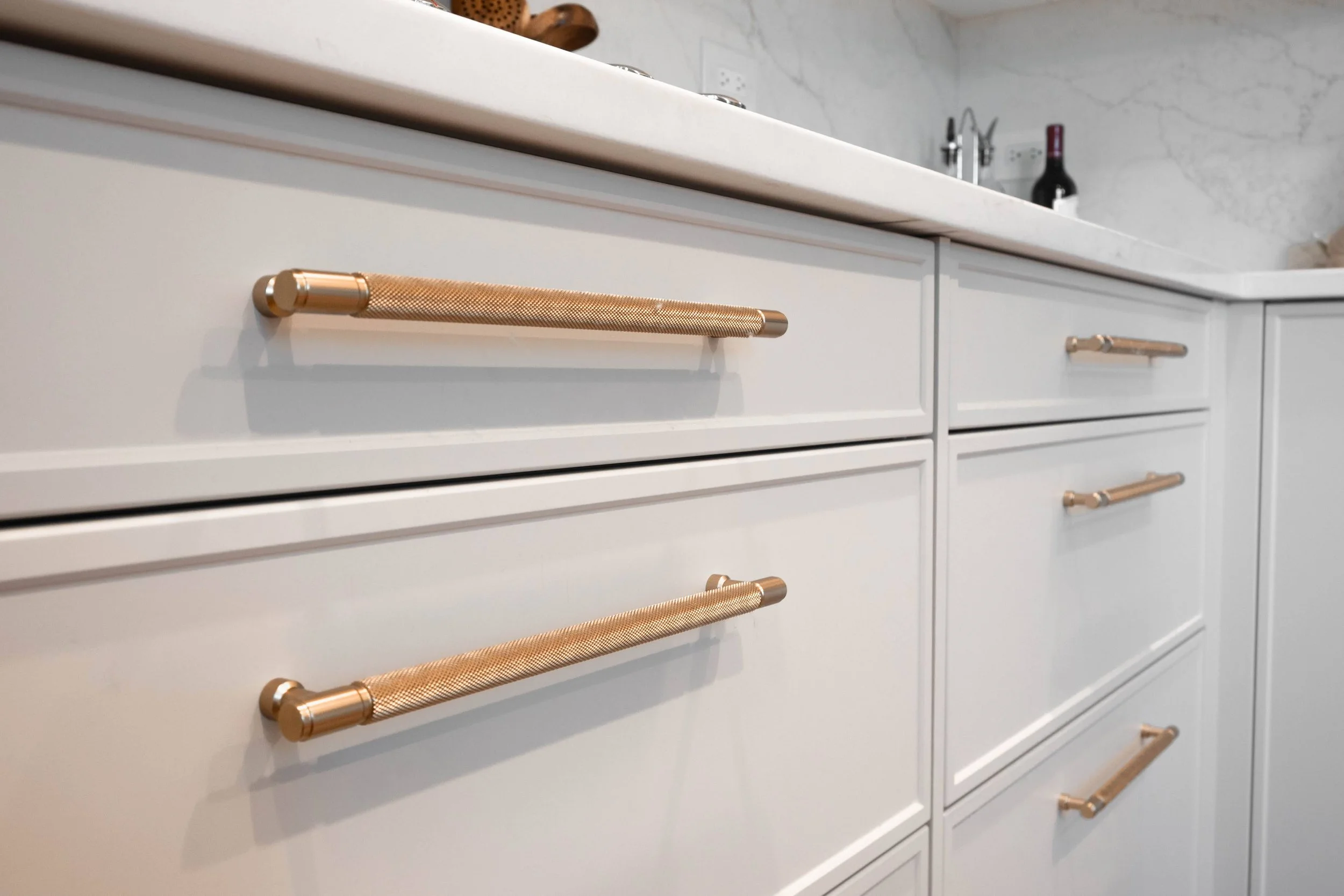 Macro detail of brushed gold cabinet pulls, offering a warm, luxurious contrast against the crisp white painted finishes.