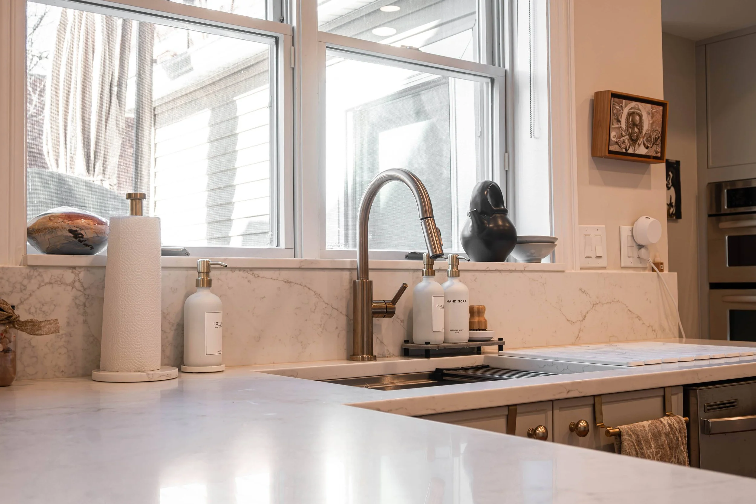 A high-end modern kitchen faucet and sink setup, highlighting clean lines and the bright, airy atmosphere created by natural window light.