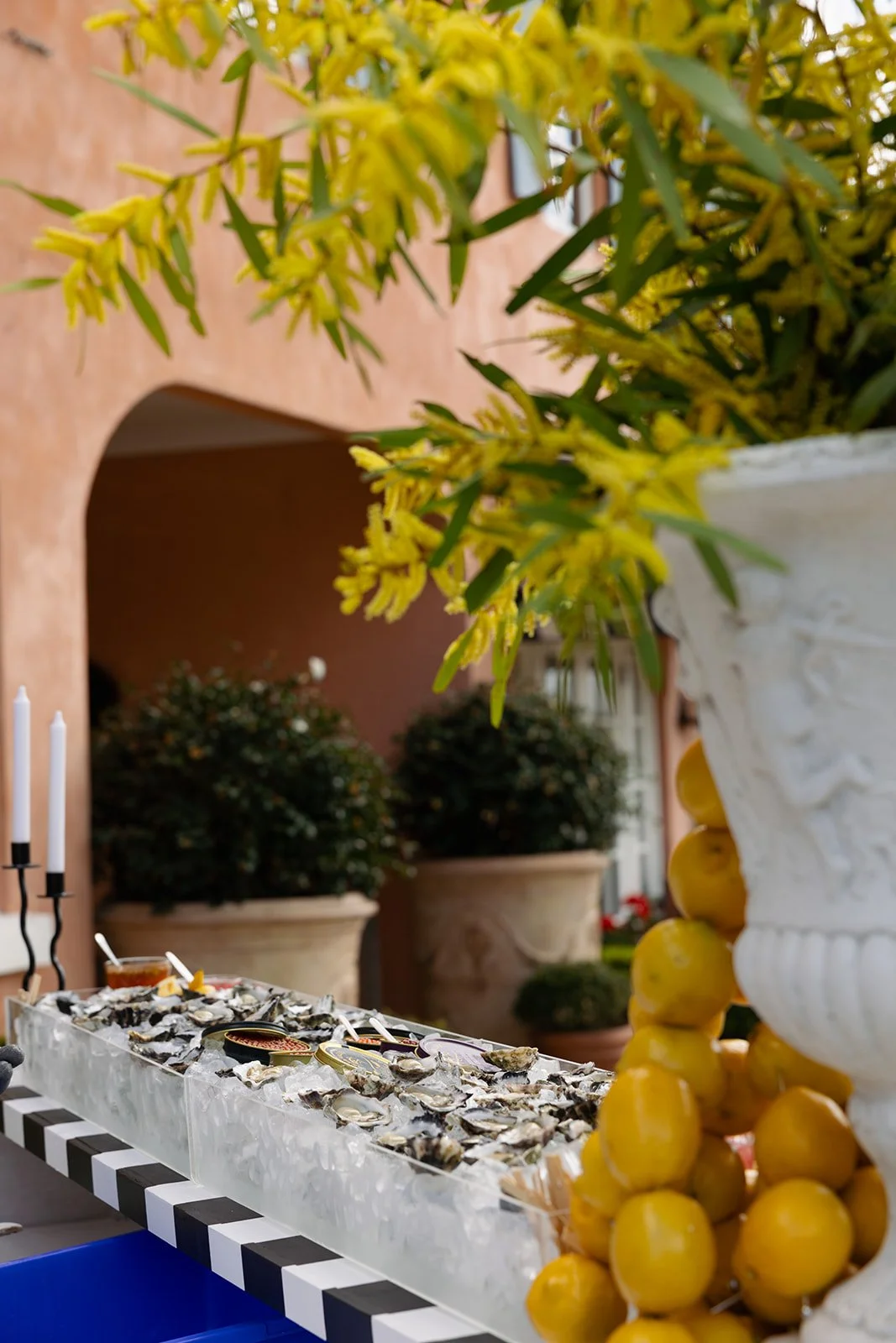 Close-up of a floral arrangement with yellow flowers in a white decorative vase, with a display of oysters on ice in the background.