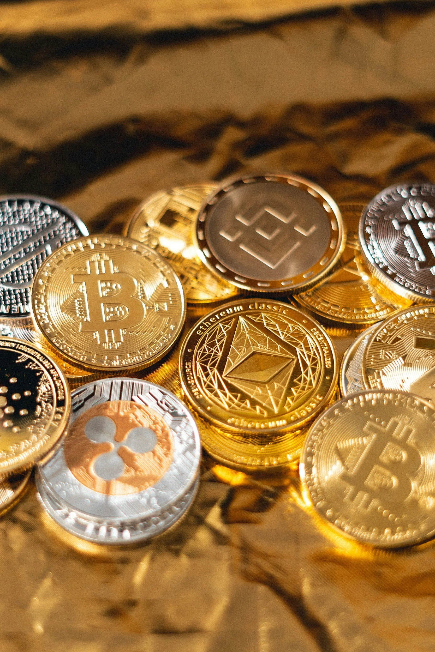 Close-up of various cryptocurrency coins, including Bitcoin, Ethereum, and Ripple, stacked on top of each other on a reflective surface.
