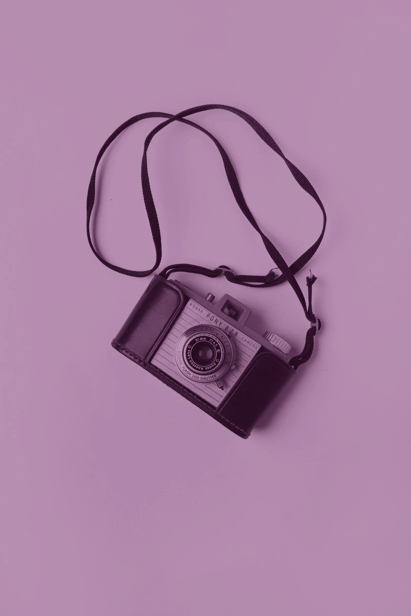 A vintage Kodak Pony 828 camera with a strap, placed on a purple background.