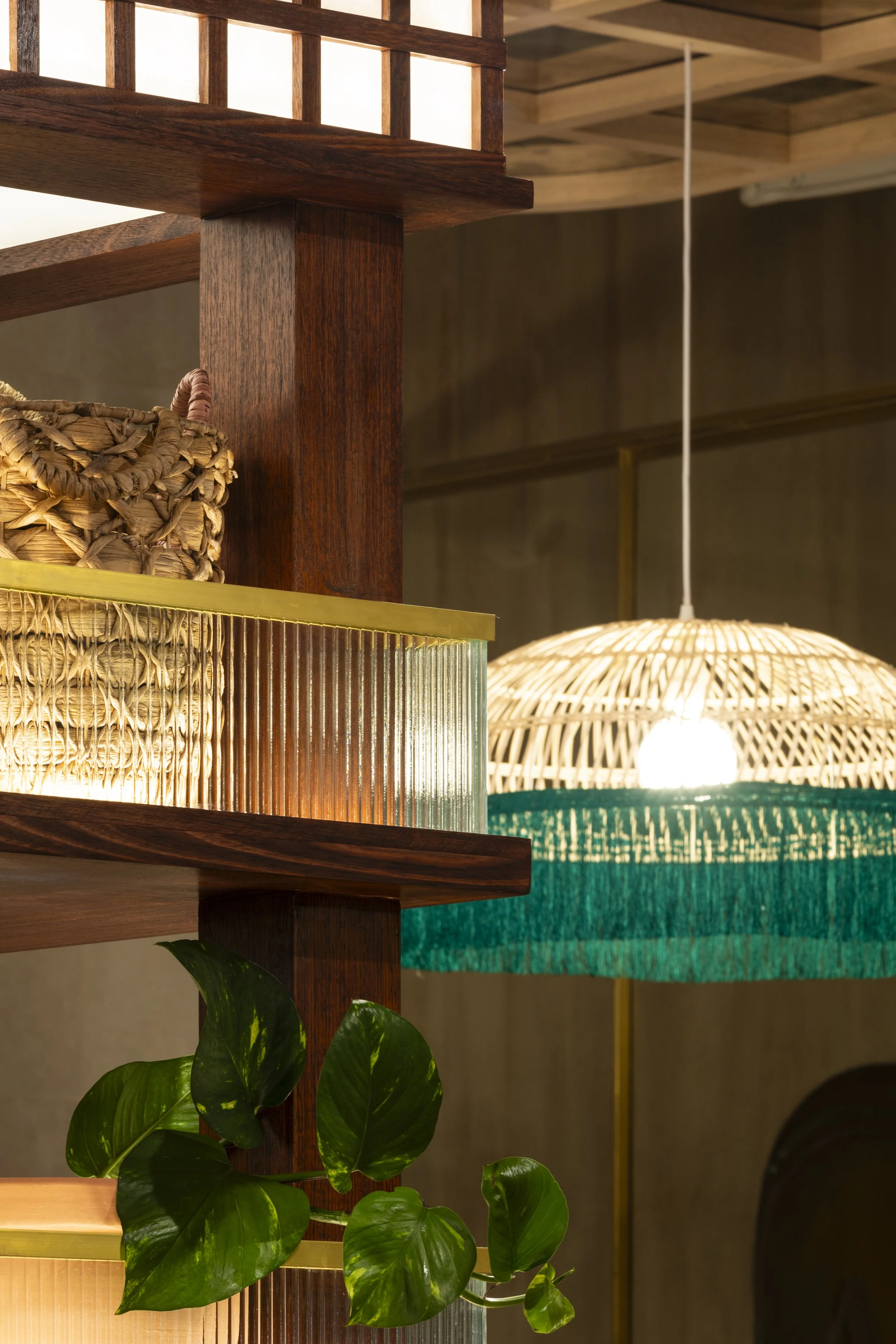 Interior view of a room with wooden shelving, a woven basket, a green leafy plant, and a hanging lampshade with a woven design and teal trim.