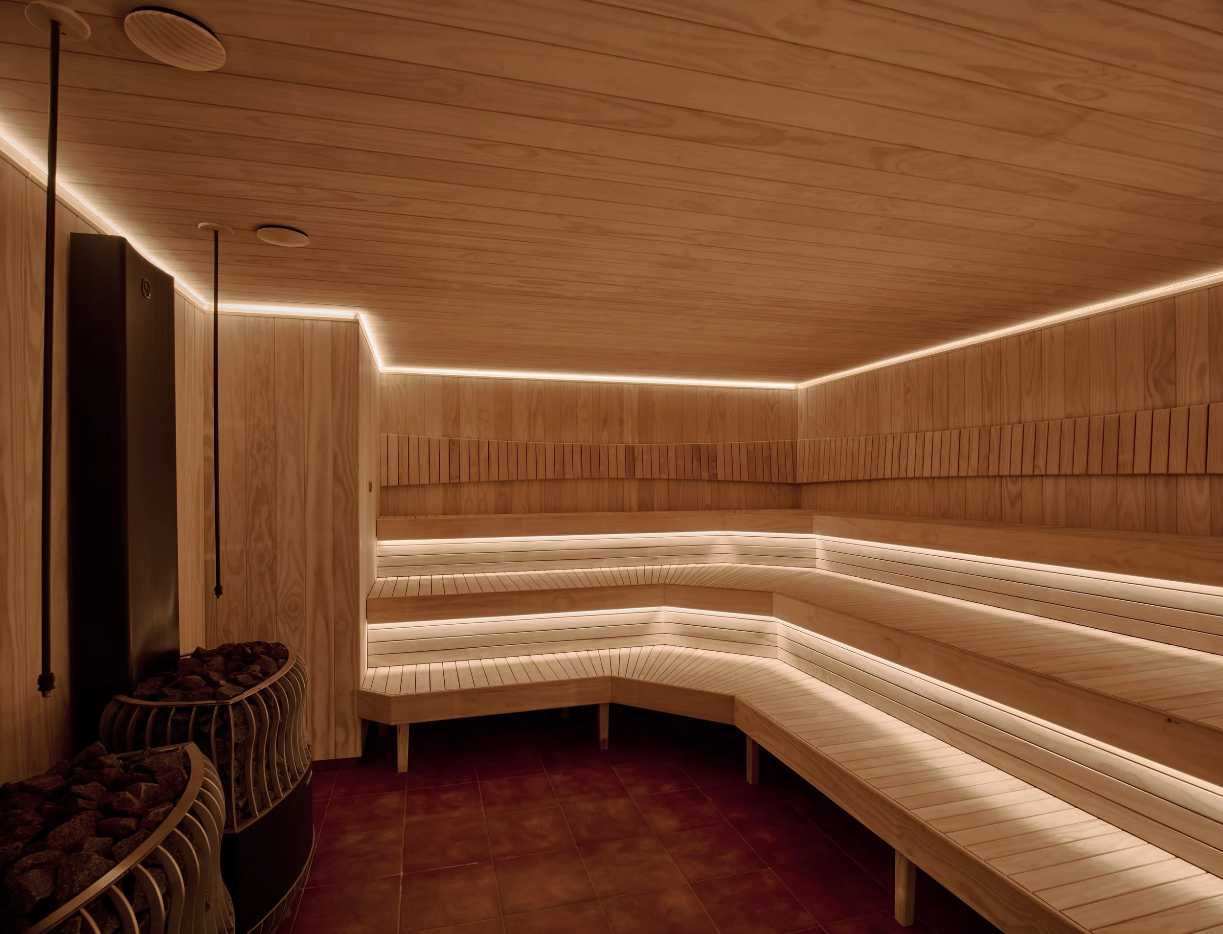 Wood-paneled sauna room with tiered benches and a fire pit with rocks for heat on the left side.
