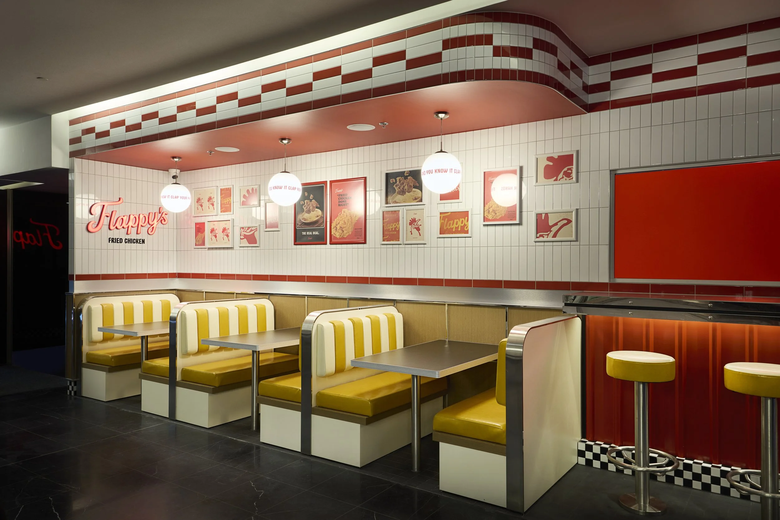 Interior of a fast-food restaurant, featuring yellow and white booth seating, red and white tiled decor, framed posters on the wall, and bright lighting.