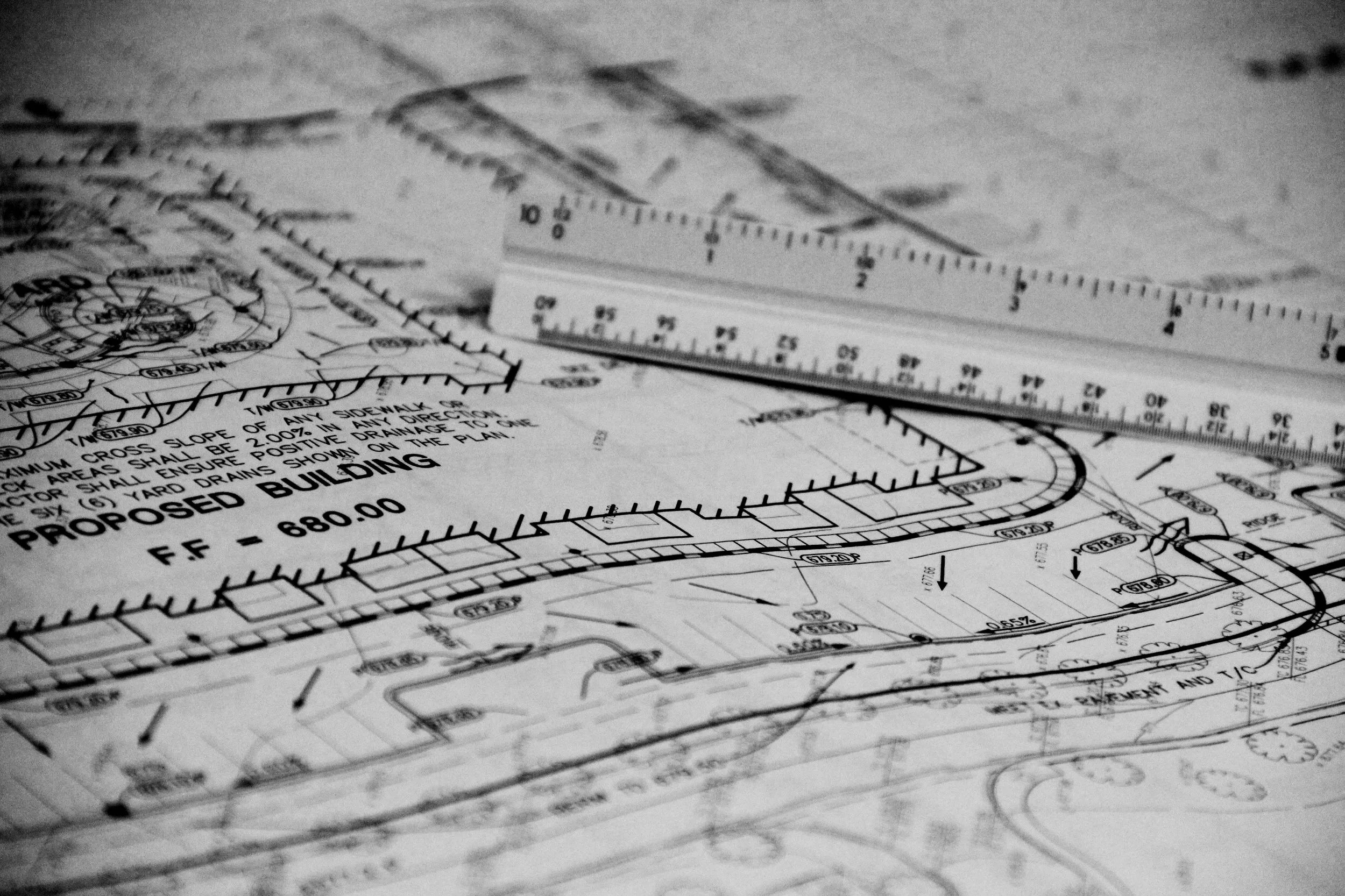 Black and white photo of an architectural blueprint with a metal ruler on top.