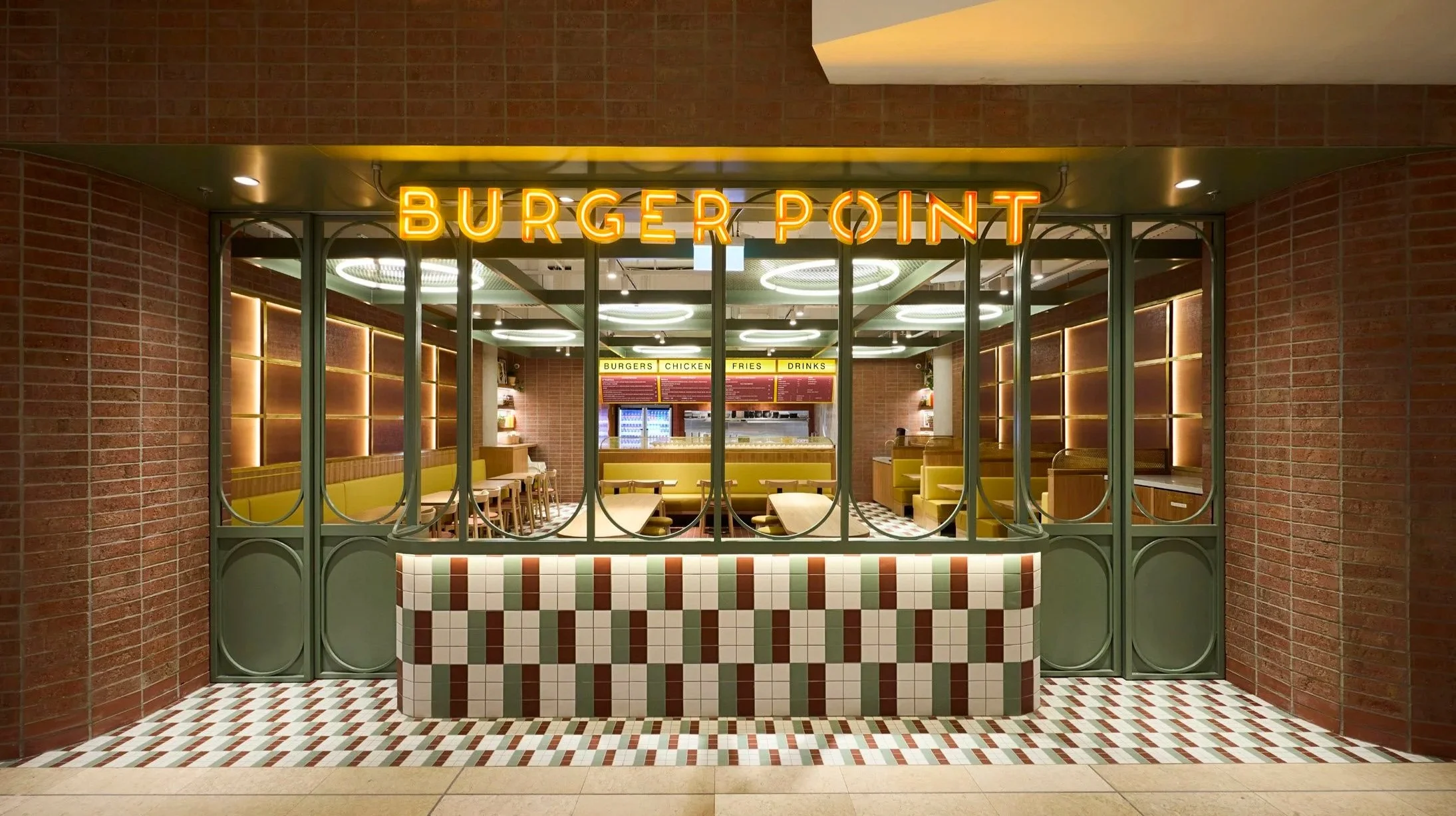 Front view of a Burger Point restaurant with a neon sign, interior seating with yellow booths, brick walls, and a tiled floor.