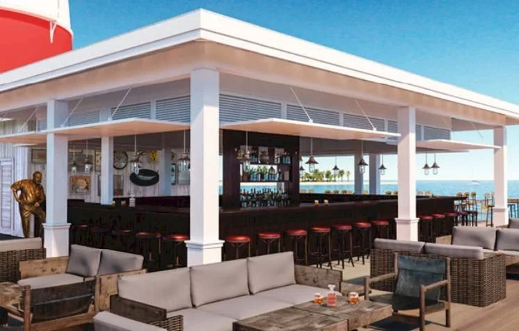 Outdoor bar and seating area with couches and chairs at a seaside restaurant or lounge on a sunny day.