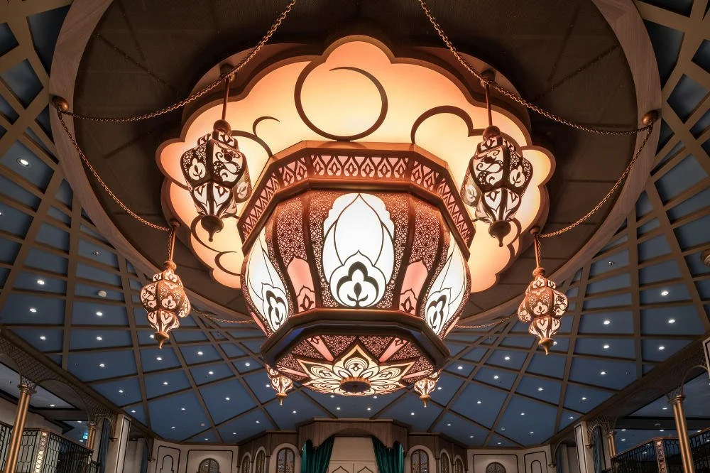 Intricate ceiling light fixture with warm glowing lampshades and decorative hanging lanterns in a spacious, ornately decorated room.