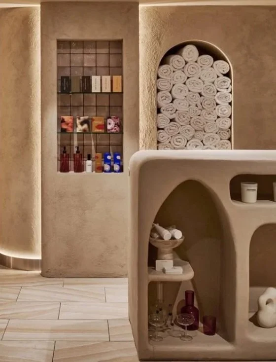 Spa or wellness center with shelves of towels, skincare products, and decorative items in a softly lit, neutral-colored room.