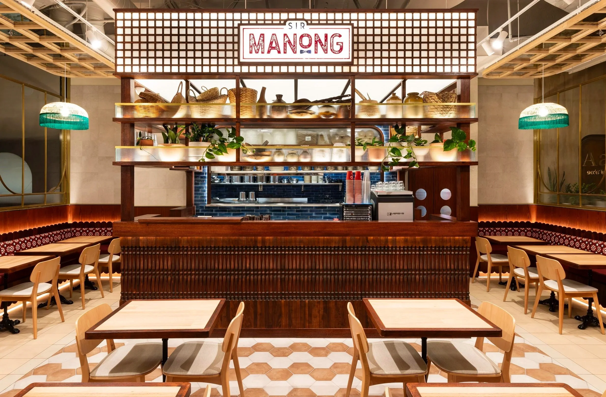 Interior of a restaurant with wooden tables and chairs, decorative lighting, and a counter with a sign that says 'Sir Manong'.