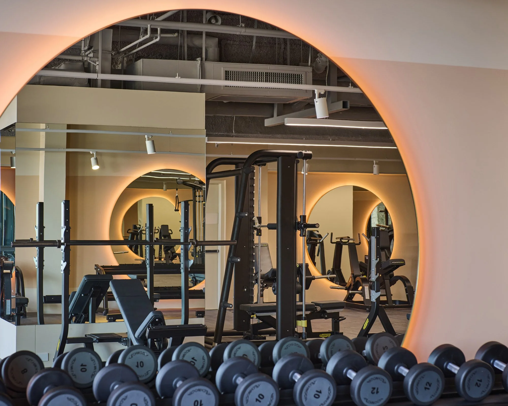 Modern gym with workout equipment, guitars, and circular mirrors with warm lighting.