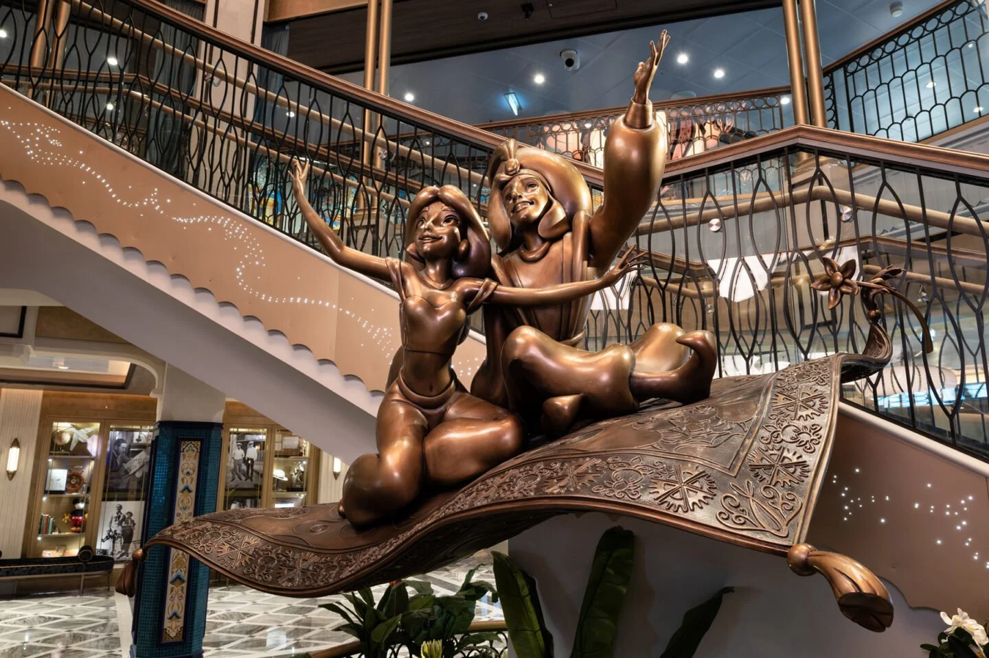 Bronze sculpture of two children sitting on a large, ornate book with a decorative cover, placed in a hotel lobby.