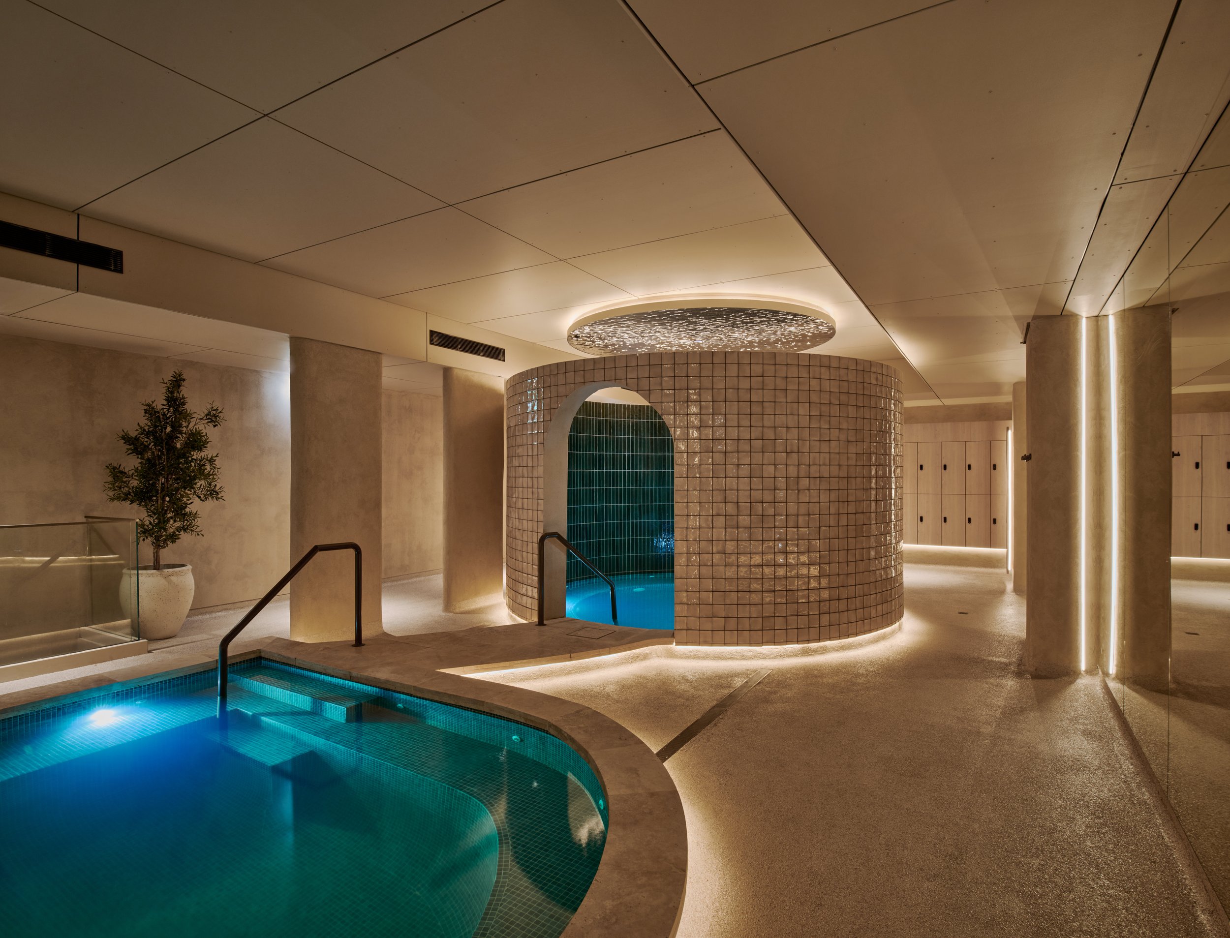 Indoor spa with a small pool, a circular tiled hot tub, modern lighting, and lockers in the background.