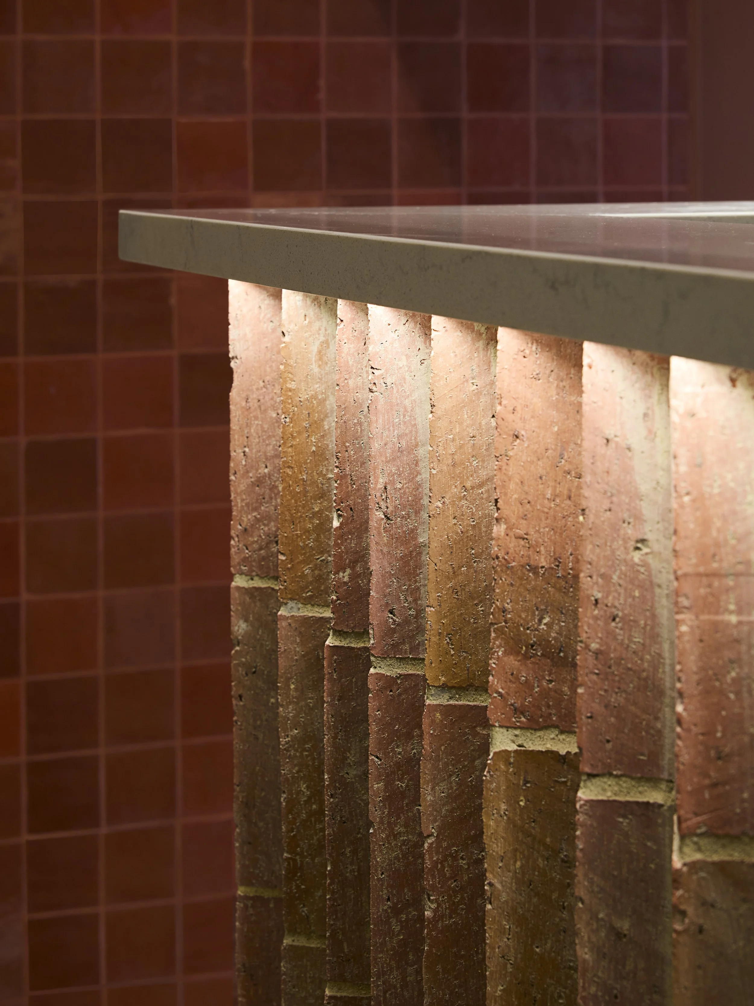 Close-up of a countertop on top of a brick support structure with a red tiled wall in the background.