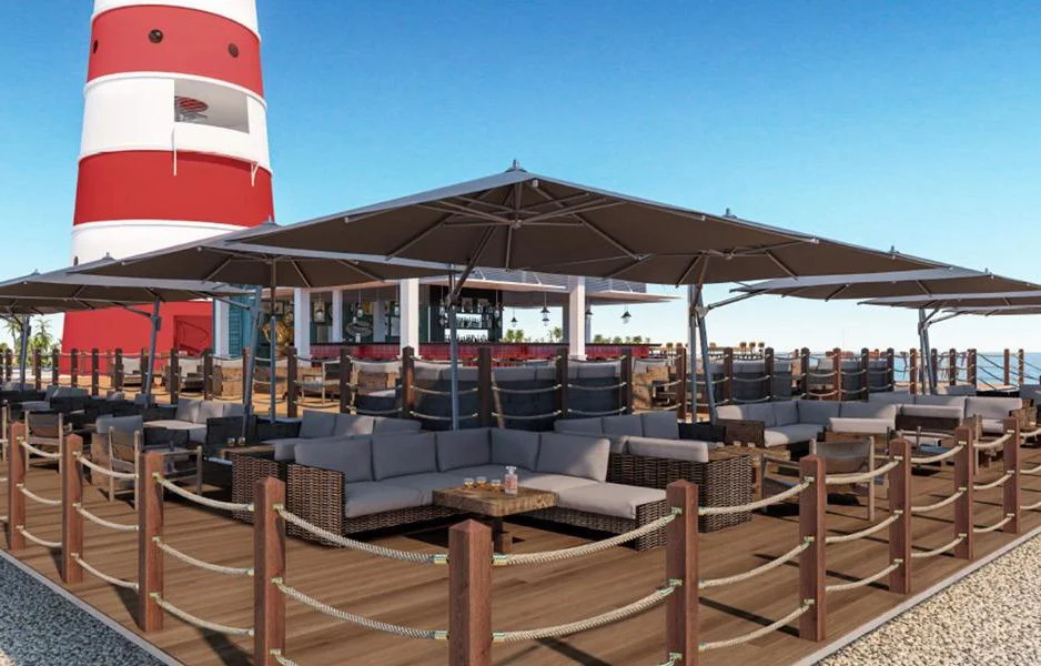 Outdoor patio with sofas and umbrellas near a lighthouse during daytime.