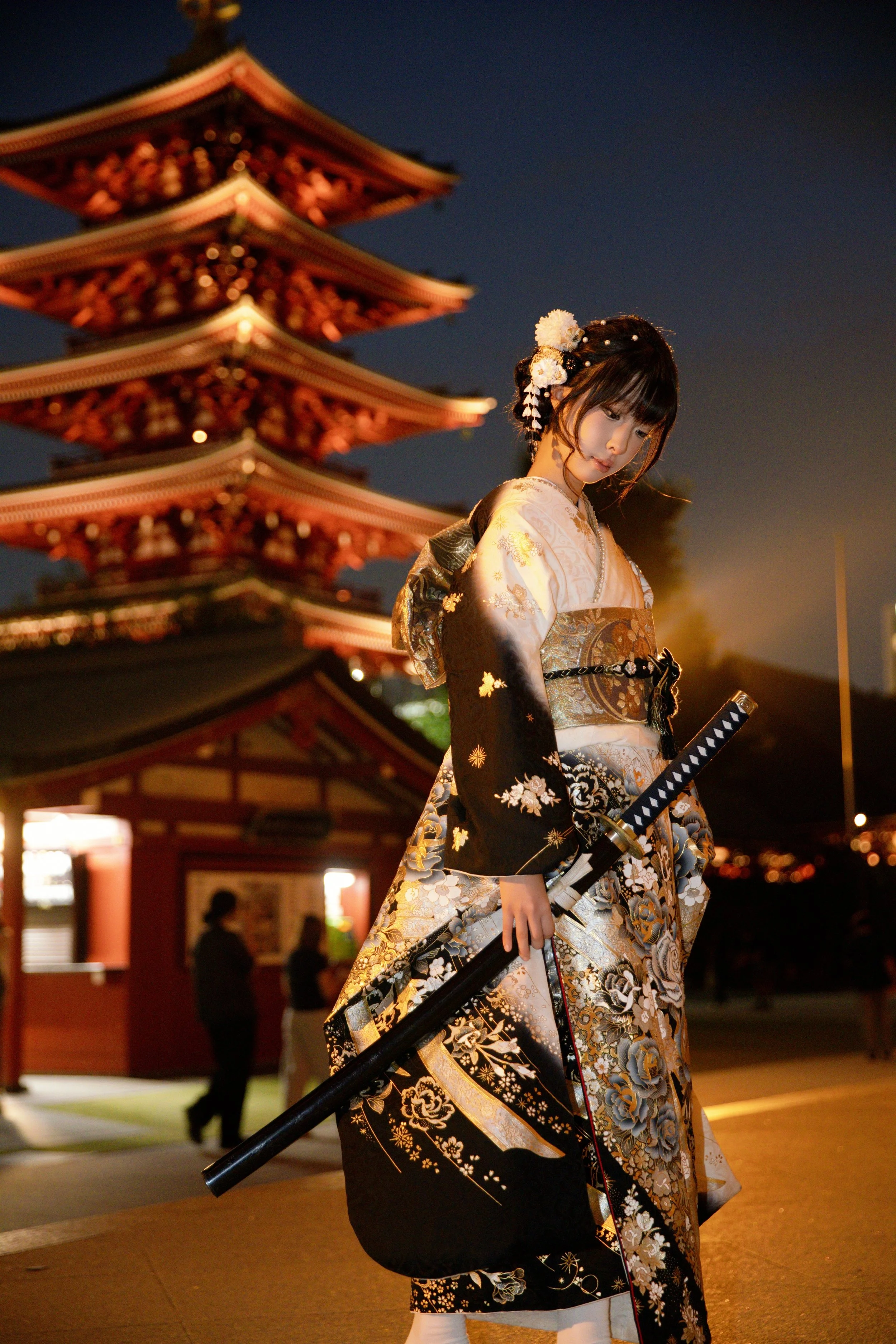A woman dressed in an elegant black and white kimono with gold and floral patterns, wearing large black sunglasses, and sitting in a white luxury car on a city street.
