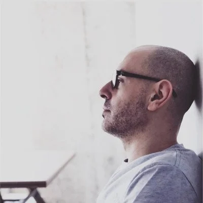 A man wearing glasses sitting and looking in profile, with a neutral expression.