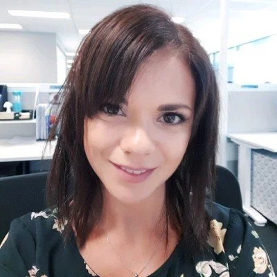 A woman with shoulder-length brown hair smiling in an office setting.