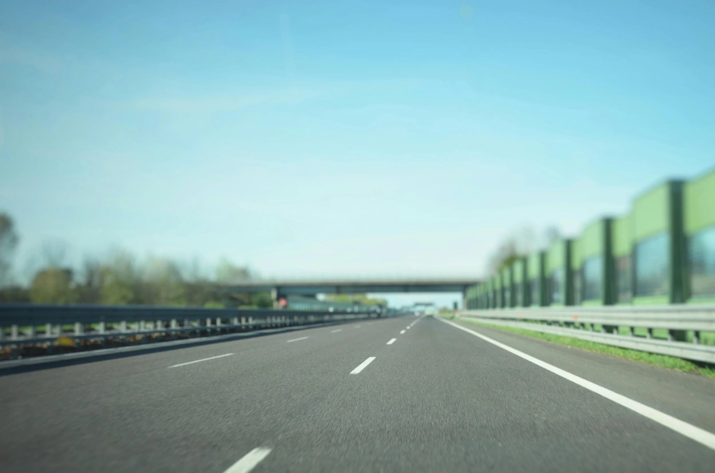 Empty highway with green sound barriers and a blue sky.