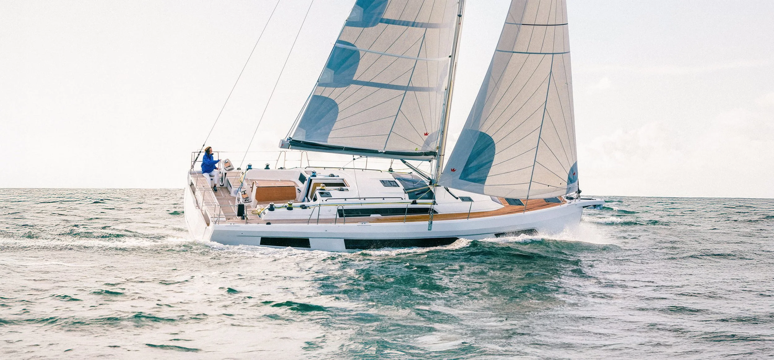 A large sailboat with the name DUFOUR 44 is on display at an indoor boat show. The boat is elevated on supports and has a sleek, modern design with a white hull decorated with blue and yellow accents. Signage below the boat reads 'Instinctive Sailing'.