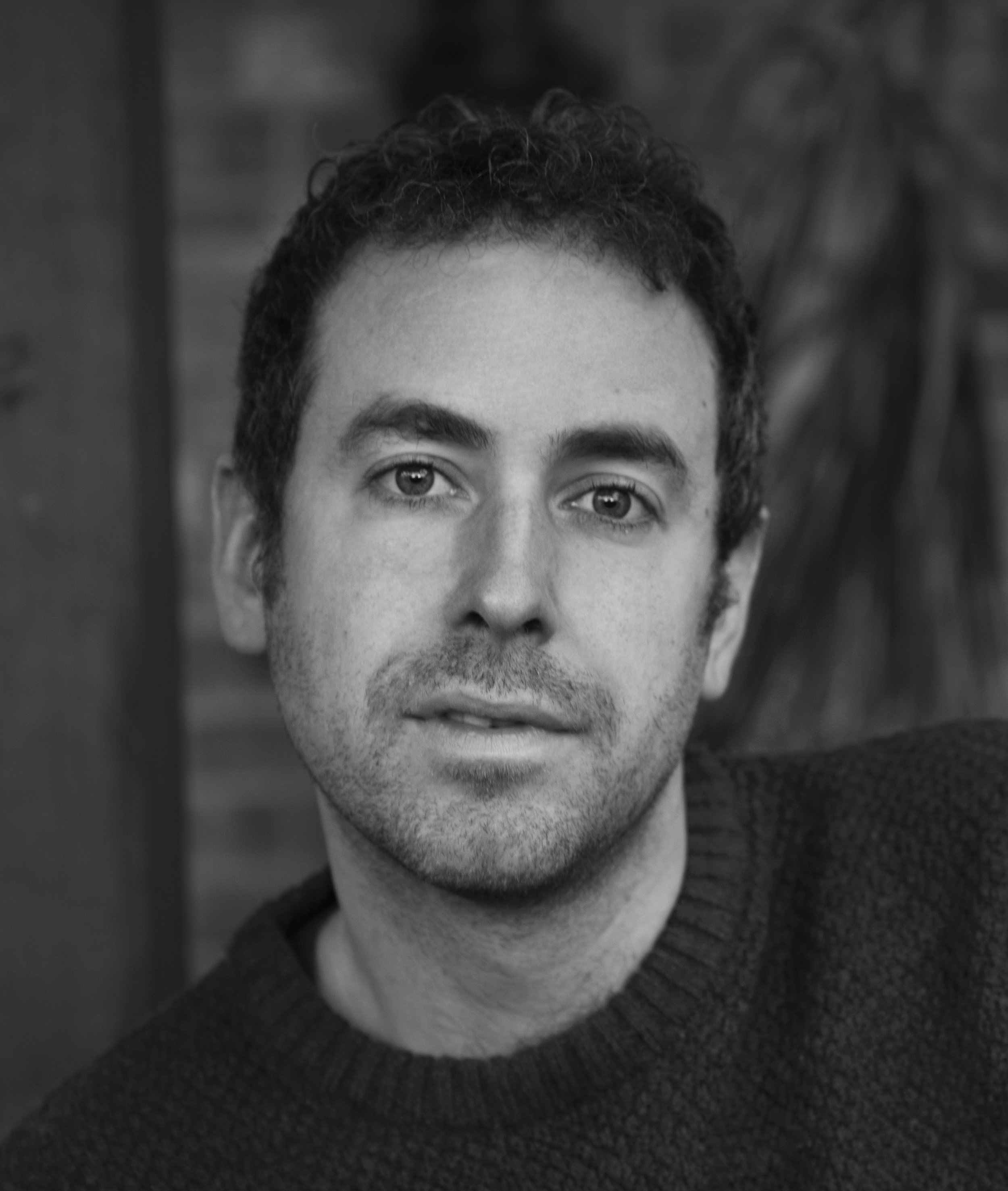 Close-up black and white photo of a man's face, focusing on his eyes, nose, mouth, and short curly hair.